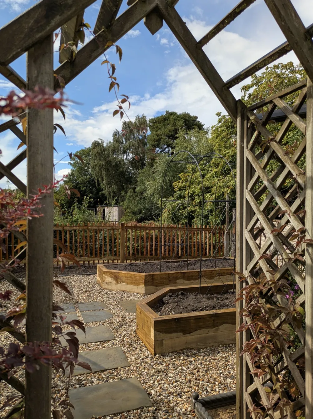 View through a timber pergola to sleeper raised beds and steel growing arches